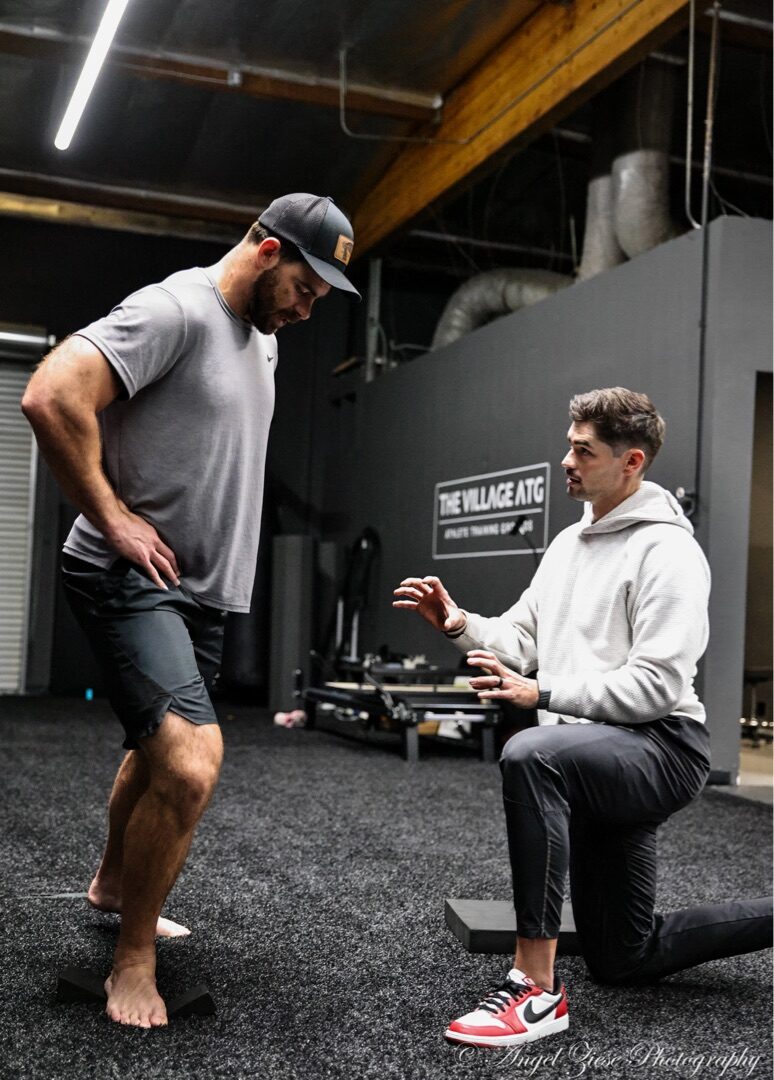 Dr. Tyler Slamans coaching an athlete through a performance therapy movement assessment at The Village ATG