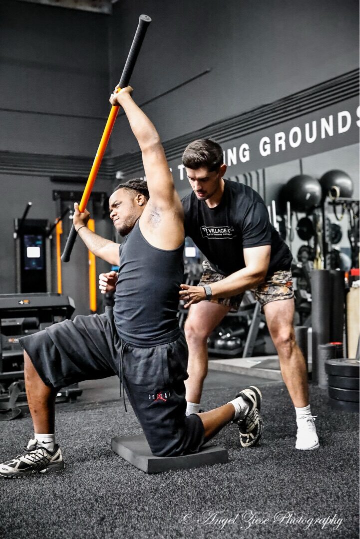 Dr. Tyler Slamans guiding an athlete through a half-kneeling shoulder mobility movement assessment